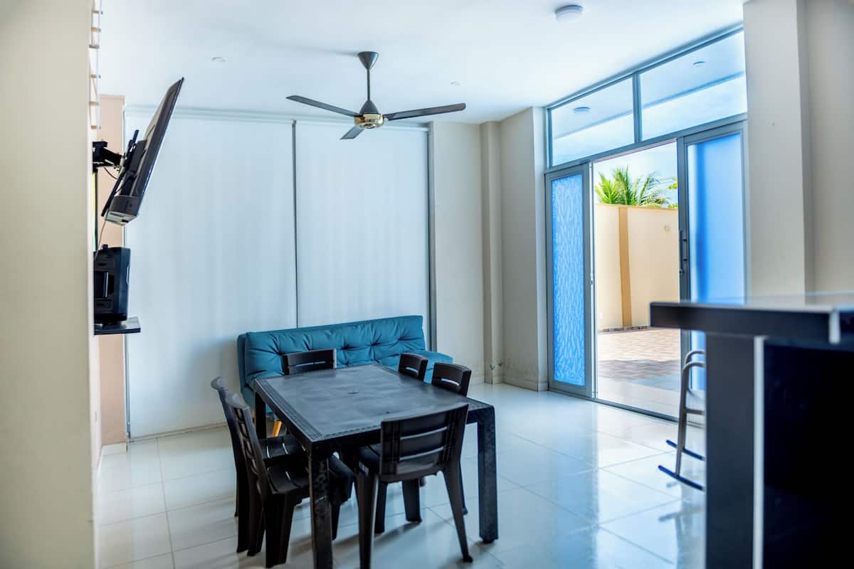 Comedor con mesa y sillas, ventilador de techo y vista a través de un ventanal.