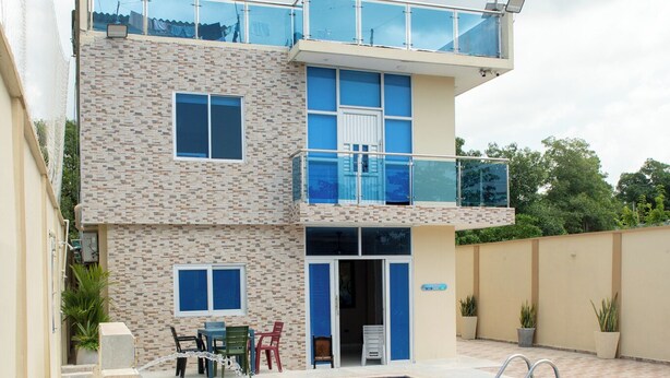Una casa de dos pisos con piscina, un balcón y un patio con mobiliario exterior.