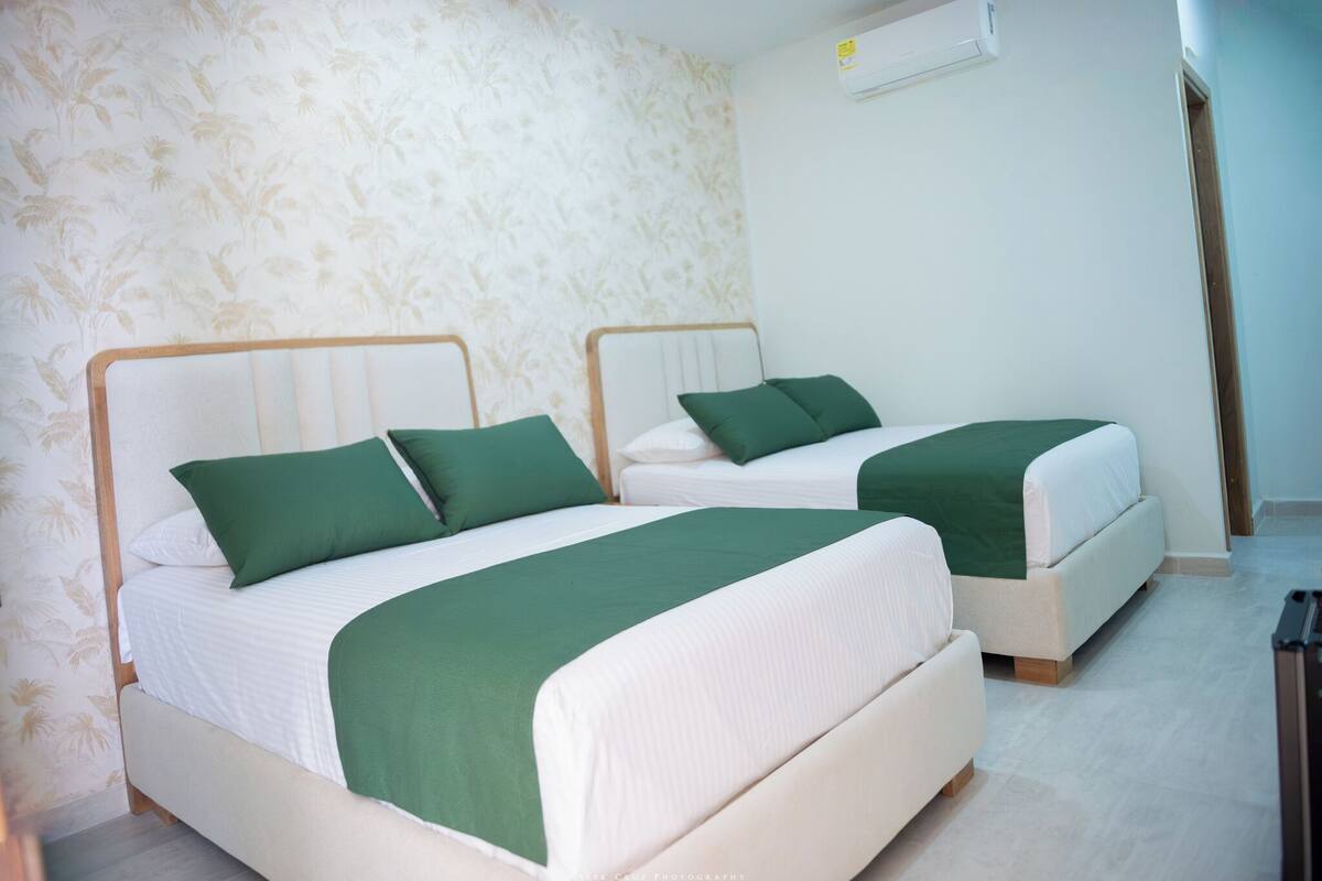 Una habitación de hotel con dos camas, cada una con ropa de cama verde y cabeceros blancos.