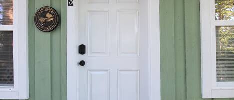 A green house with a white door, number 3, and a welcome mat.