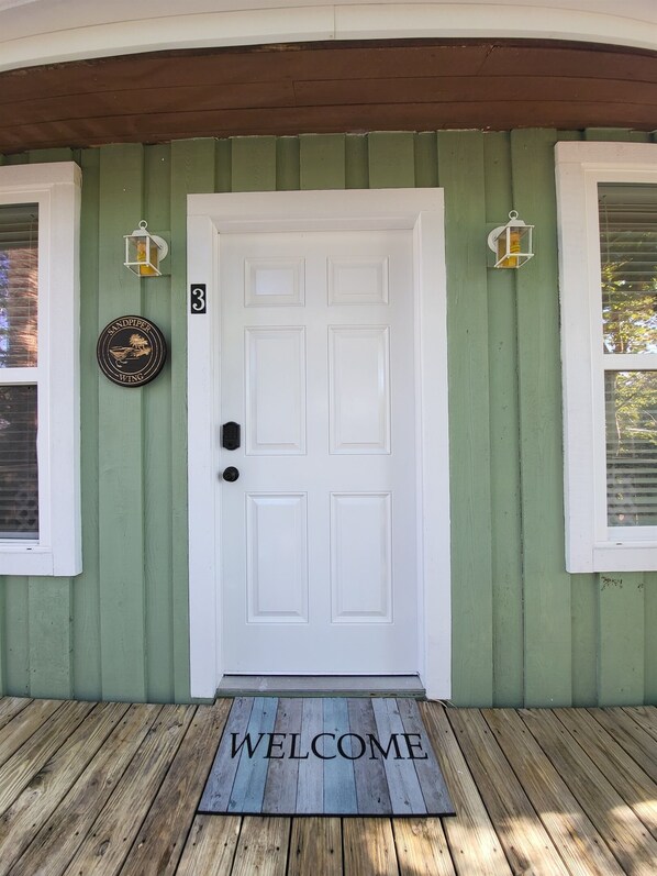 A green house with a white door, number 3, and a welcome mat.