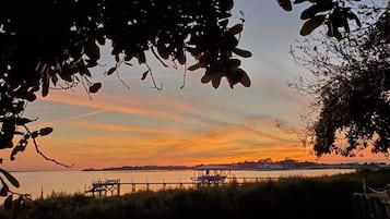 Une vue sur le coucher de soleil, avec un plan d’eau calme, un quai et une rive éloignée.