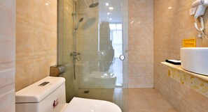 A modern bathroom with a glass-enclosed shower, a toilet, and a sink with a hairdryer on the wall.