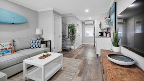 A modern living room with a sofa, coffee table, and a surfboard decoration. - Beachside! Jacksonville Beach Condo-Close to Mayo Clinic (Jacksonville Beach)