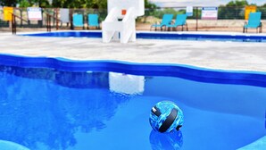 A swimming pool with a blue ball, white lounge chairs, and a white chair in the background. - Son's Rio Cibolo - Glamping Cabin G (Marion)