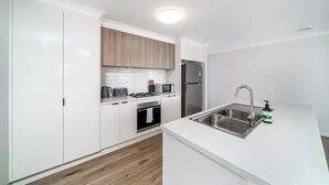 A modern kitchen with white cabinetry, a stainless steel sink, and a built-in oven. - Modern Escape in Quiet Neighbourhood (Gobbagombalin)
