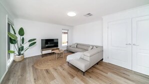 A modern living room with a sofa, TV, and a large plant. - Modern Escape in Quiet Neighbourhood (Gobbagombalin)