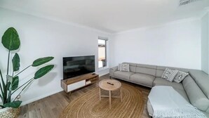 A modern living room with a flat-screen TV, a sofa, a coffee table, and a large plant. - Modern Escape in Quiet Neighbourhood (Gobbagombalin)