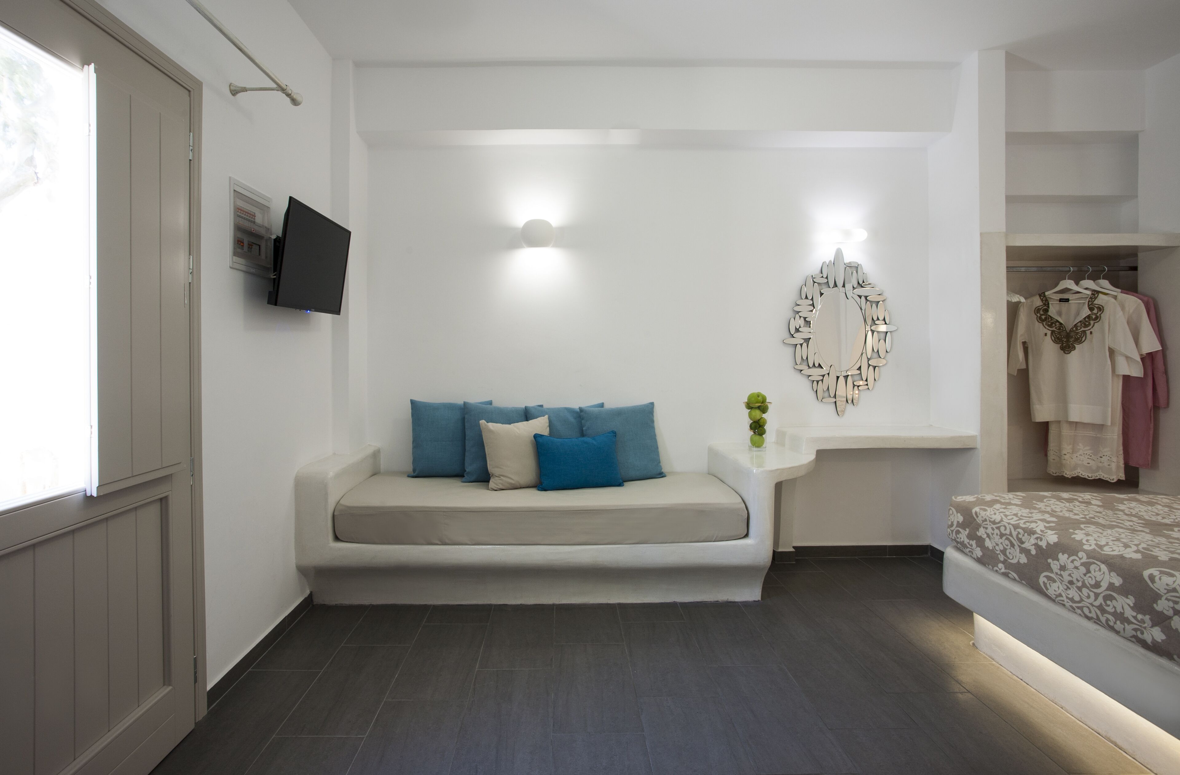 A modern bedroom with a sofa bed, a flat-screen TV, a wall-mounted mirror, and a clothing rack.
