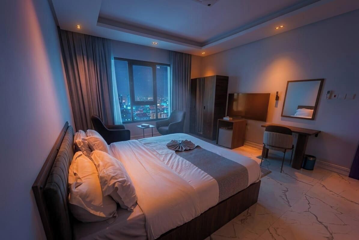 Hotellihuone, jossa on suuri sänky, työpöytä, tuoli, peili ja näkymä kaupunkiin yöllä.