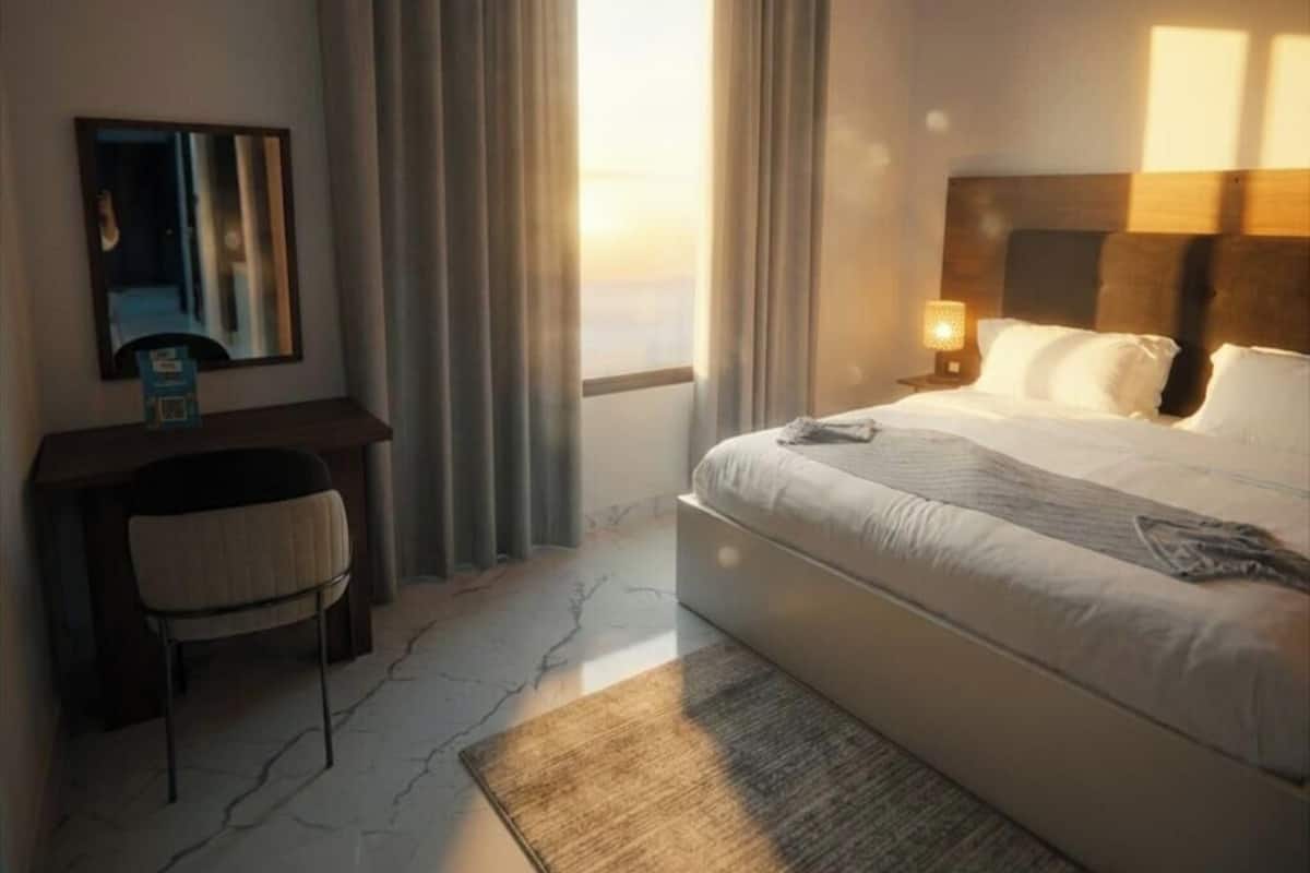 A hotel room with a bed, a desk, a chair, a mirror, and a window with curtains.