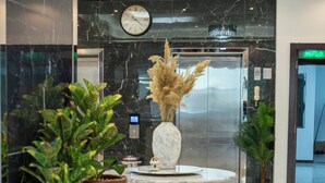 Un vestíbulo con piso de mármol, una mesa redonda con un jarrón de flores secas y plantas en macetas.