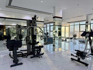 A modern gym with various exercise equipment, large windows, and a polished marble floor.