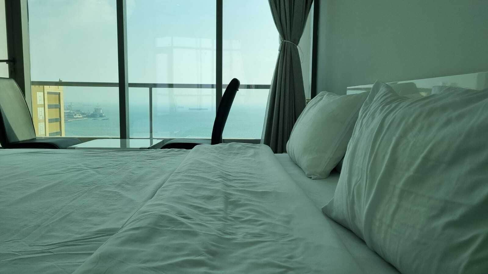 A hotel room with a large bed, a view of the city through floor-to-ceiling windows, and a chair by the window.