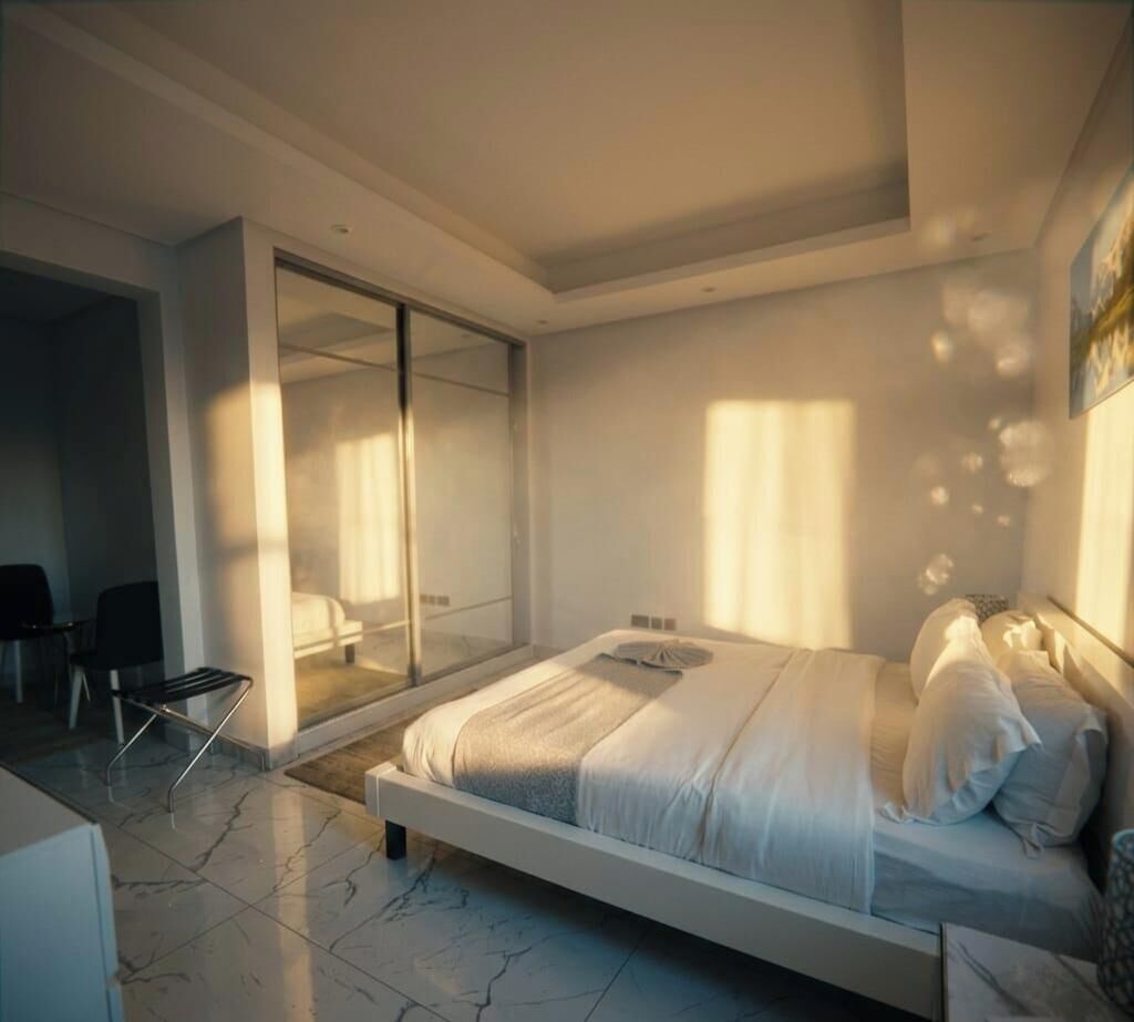 A modern bedroom with a large bed, a sliding glass door leading to a balcony, and a separate seating area.