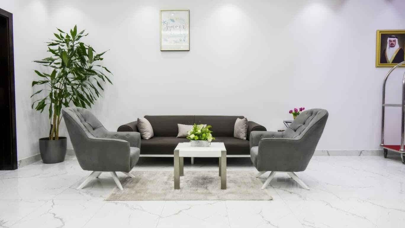 Una sala de estar moderna con un sofá oscuro, dos sillones grises, una mesa de centro blanca y una planta grande en maceta.
