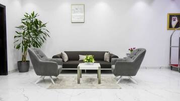 Una sala de estar moderna con un sofá oscuro, dos sillones grises, una mesa de centro blanca y una planta grande en maceta.
