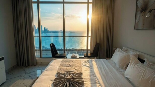 Habitación de hotel con una cama grande, dos sillas y vistas al horizonte de la ciudad, además de un ventanal amplio.