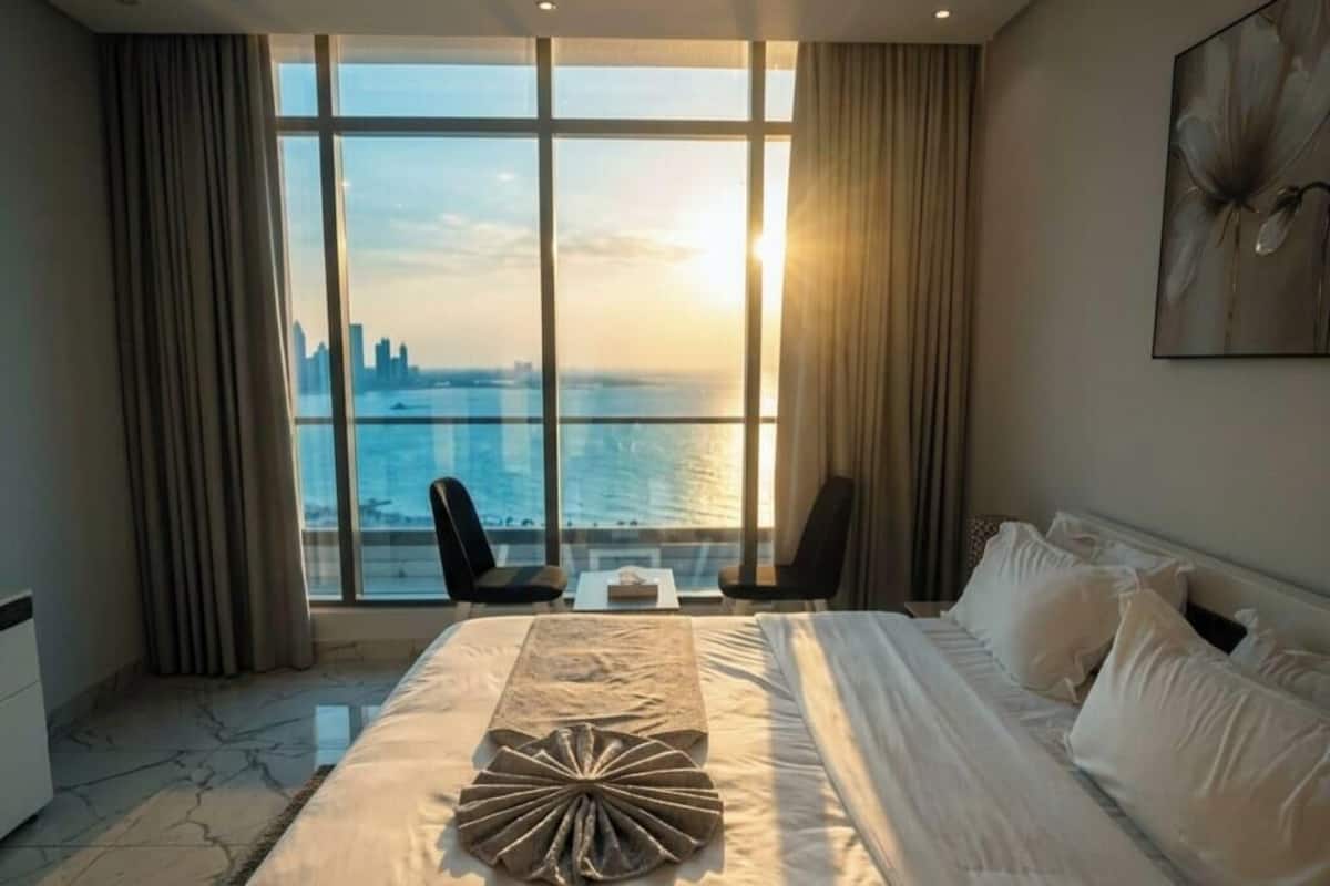 A hotel room with a large bed, two chairs, a view of the city skyline, and a large window.