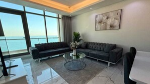Una sala de estar moderna con un ventanal grande con vistas al mar, un sofá seccional gris, una mesa de centro de vidrio y un estilo de decoración minimalista.