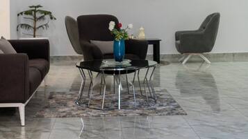 A modern, spacious lobby with a marble floor, two dark armchairs, a glass coffee table with a vase, and a ceiling-mounted air conditioning unit.