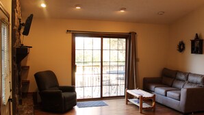 A living room with a stone wall, a black leather armchair, a brown leather sofa, and a wooden coffee table. - Winetrail Cabin - SIU, Giant City SP, Shawnee Forest, & Cedar Lake minutes away! (Makanda)