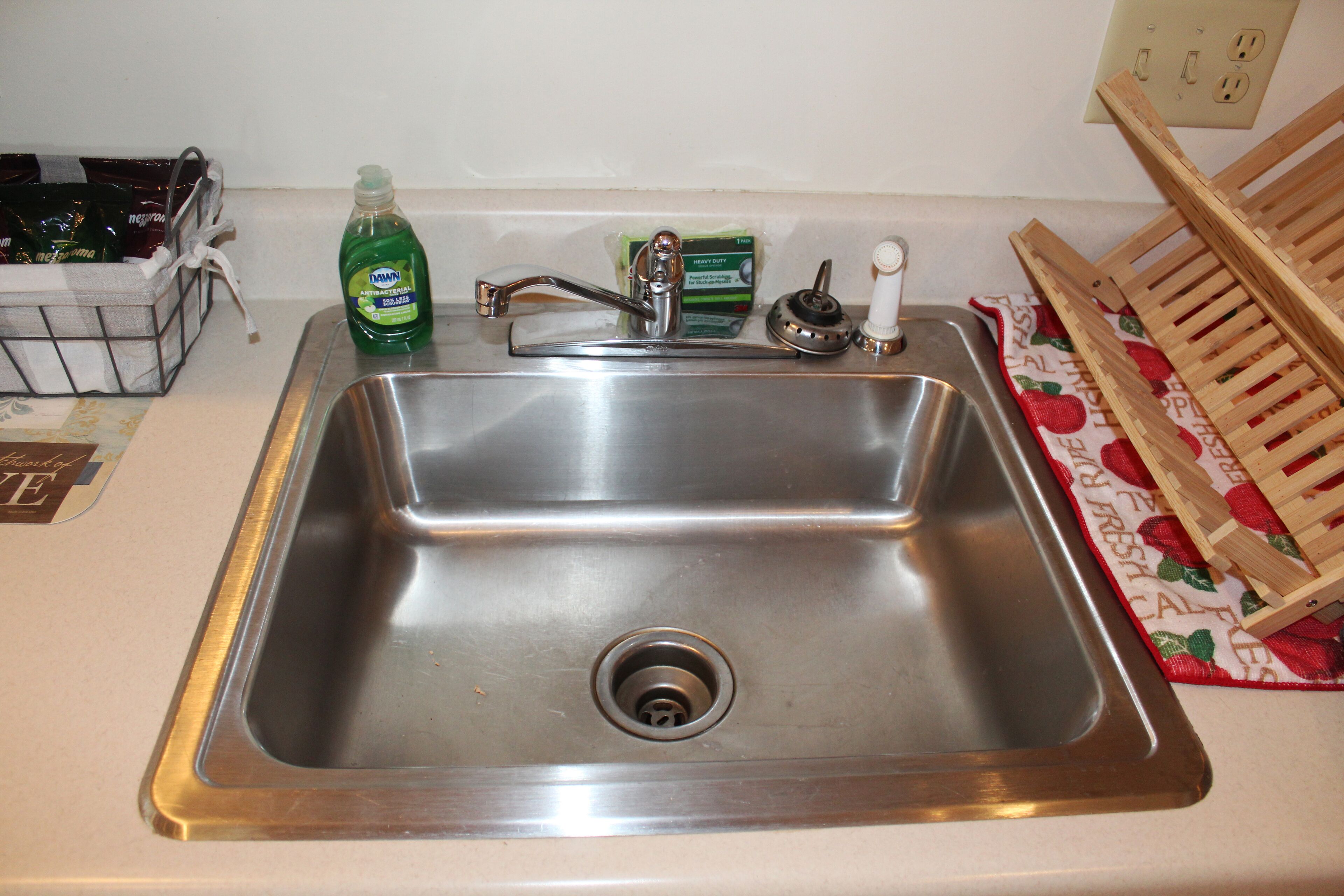 Un lavamanos de acero inoxidable con un grifo, una botella de detergente y un escurreplatos.