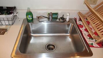 Un lavamanos de acero inoxidable con un grifo, una botella de detergente y un escurreplatos.