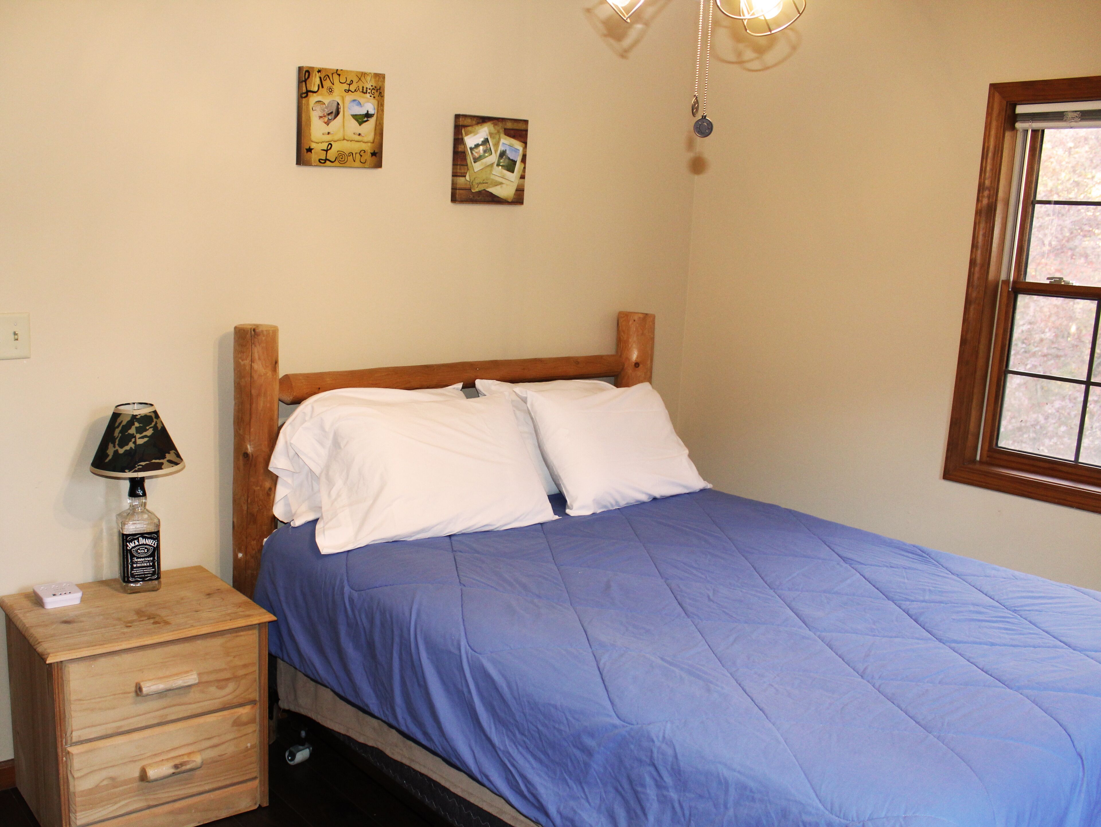Une chambre avec une tête de lit en bois, un lit simple avec une literie bleue, une lampe de chevet, une petite table de chevet en bois et deux éléments de décoration murale.