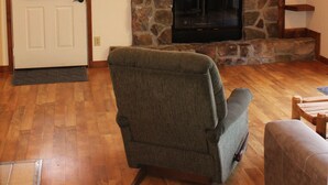 A living room with a stone fireplace, a television mounted above it, and a door with a doormat. - Winetrail Cabin - SIU, Giant City SP, Shawnee Forest, & Cedar Lake minutes away! (Makanda)