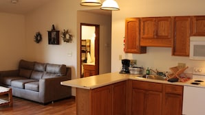 A living room with a brown leather sofa and a kitchen with wooden cabinets and a white stove. - Winetrail Cabin - SIU, Giant City SP, Shawnee Forest, & Cedar Lake minutes away! (Makanda)