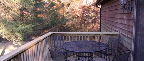 A wooden deck with a round metal table and four chairs, surrounded by trees.
