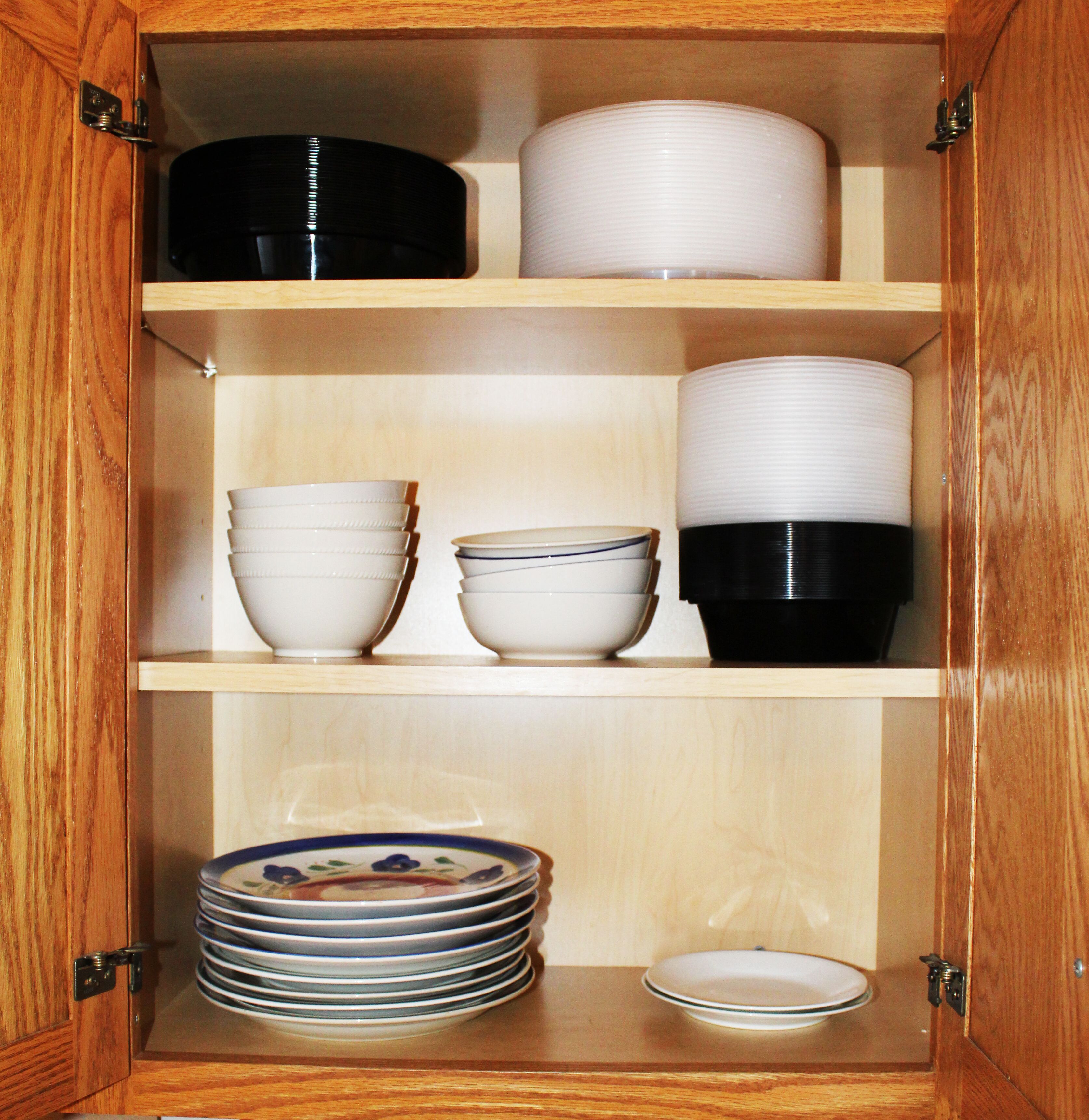 A wooden cabinet with three shelves, each containing various kitchenware items.