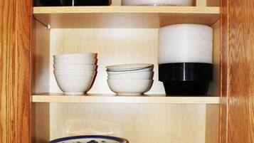 A wooden cabinet with three shelves, each containing various kitchenware items.