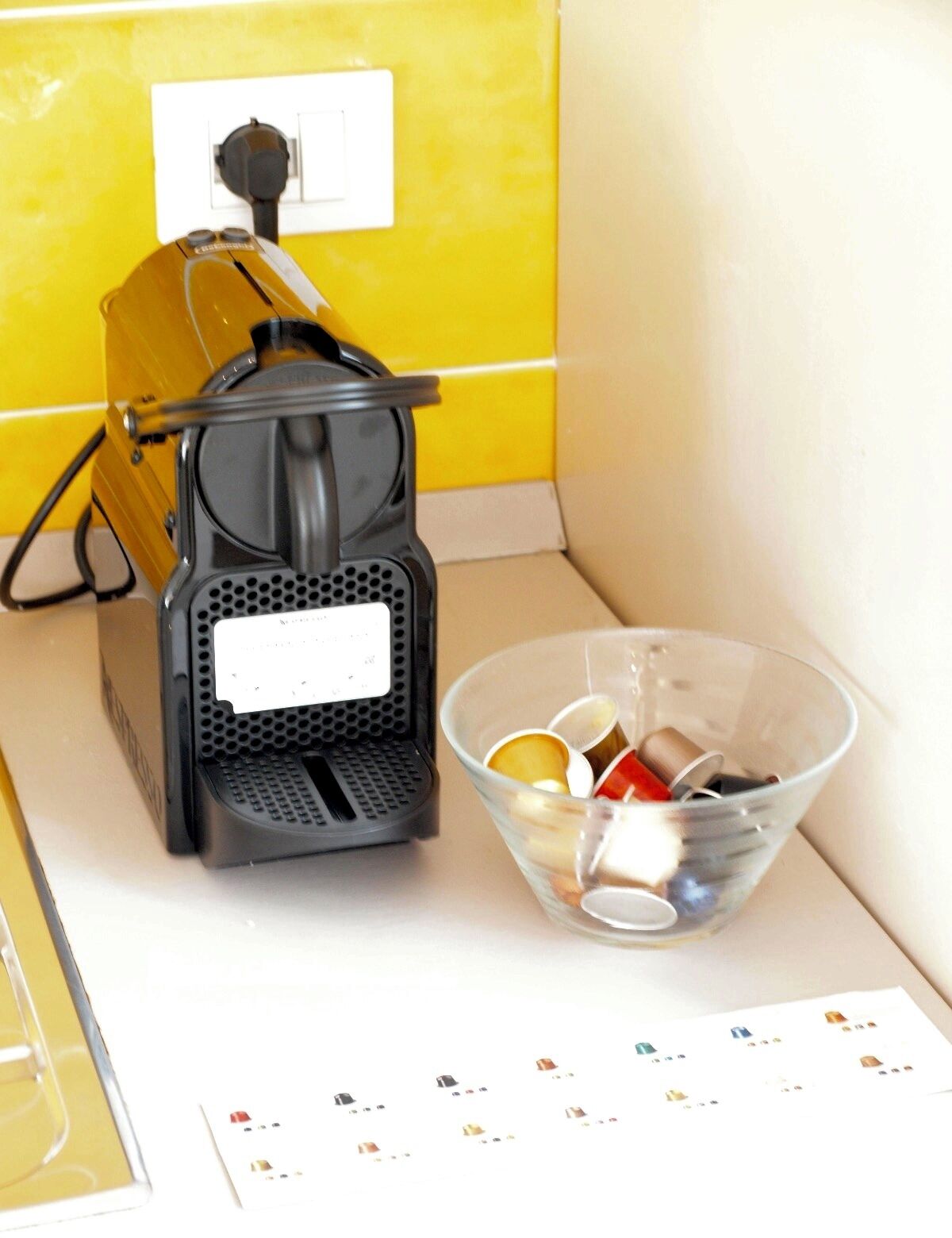 A coffee maker on a counter next to a clear glass bowl containing various coffee pods.