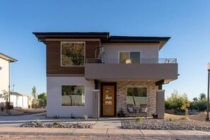 A two-story modern house with a balcony, large windows, and a stone facade.