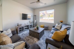 A living room with a sofa, coffee table, and TV. There's a window with a view of mountains.