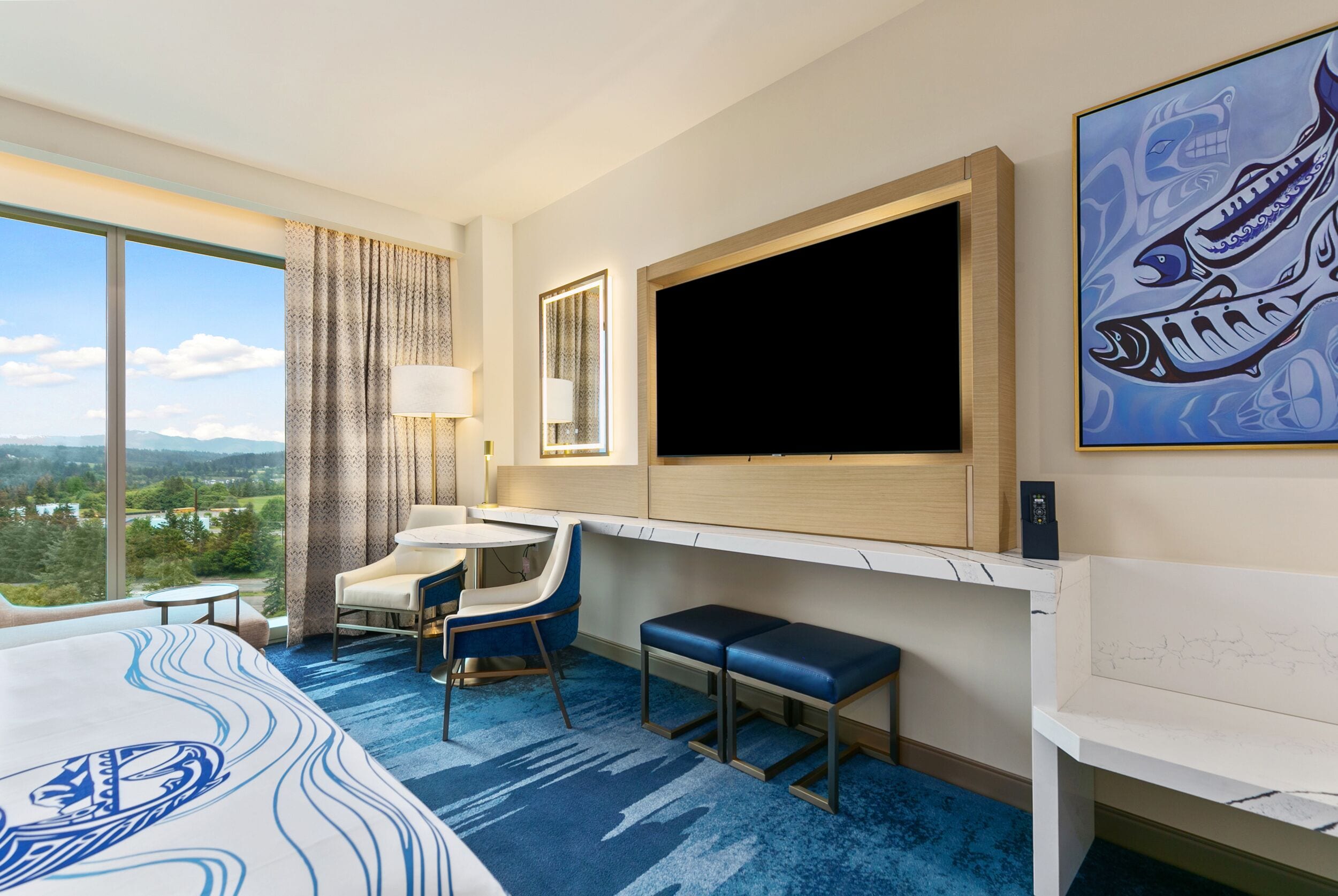 A hotel room with a large bed, a desk, a chair, a TV, and a view of the outdoors.