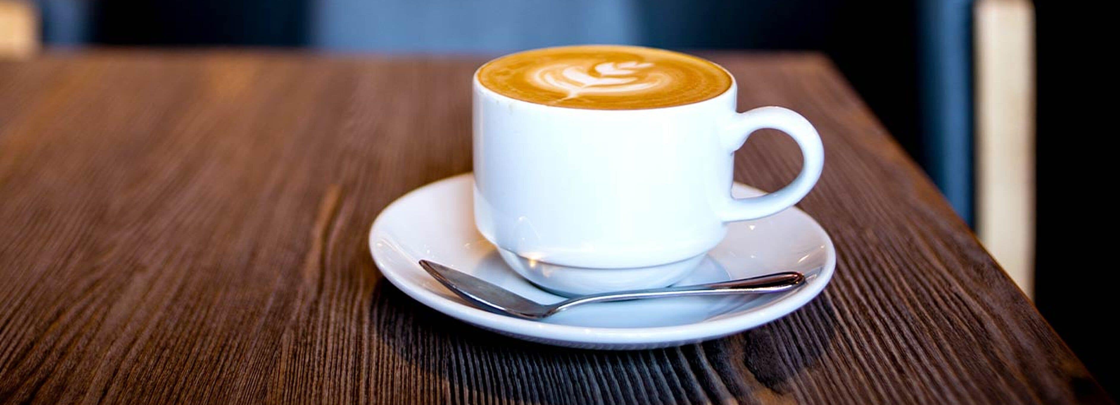 Una taza de café con leche y arte latte sobre un plato y cuchara en una mesa de madera.
