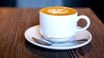 Una taza de café con leche y arte latte sobre un plato y cuchara en una mesa de madera.