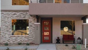 Una casa moderna de dos pisos con fachada de piedra, una puerta roja y un balcón.
