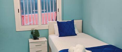 Un dormitorio con cama, ventana con vistas, una mesita de noche pequeña y aire acondicionado instalado en la pared.