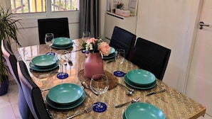 A dining table set with teal plates, glasses, and cutlery, surrounded by black chairs. A vase with flowers and a bulletin board with hanging items are visible. - RELAX HOUSE BARCELONA (Sant Esteve Sesrovires)