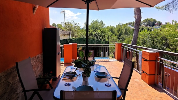 An outdoor dining area with a table set for two, surrounded by orange walls and a view of a swimming pool and greenery. - RELAX HOUSE BARCELONA (Sant Esteve Sesrovires)