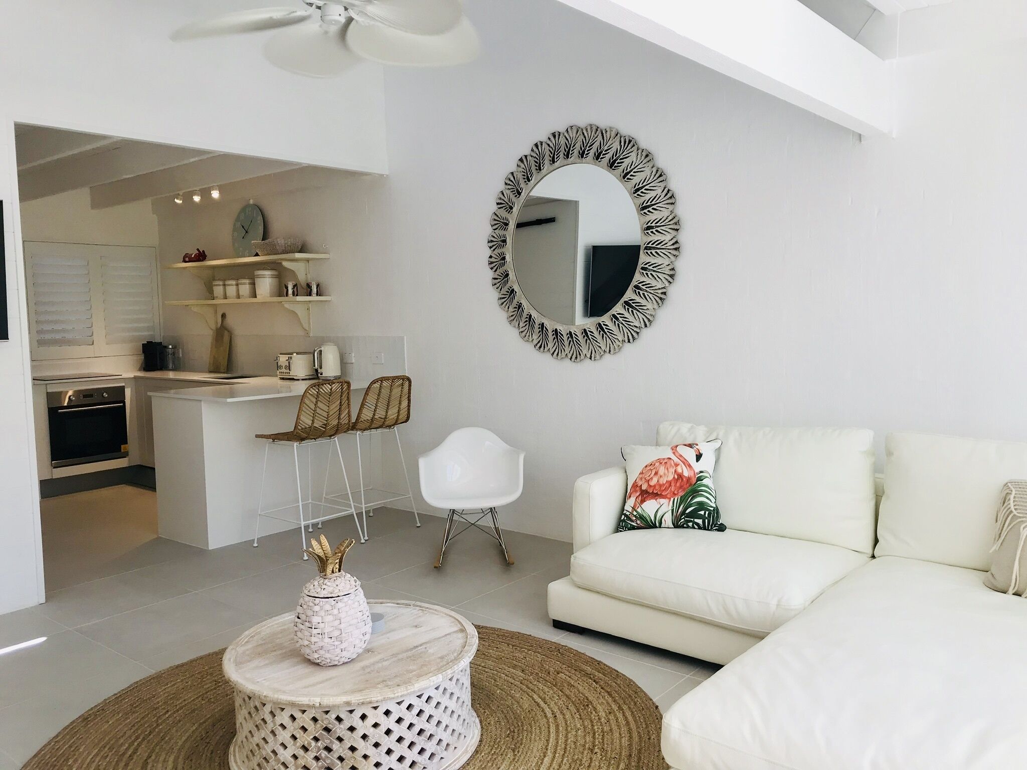 A modern living room with a white sofa, a round coffee table, and a kitchen area with white cabinets and a dining table.