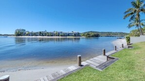 A waterfront property with a wooden dock, clear blue water, and a backdrop of buildings and greenery.