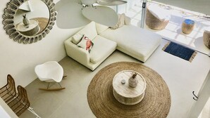 A modern living room with a white sofa, a round woven coffee table, a white armchair, and a ceiling fan.