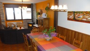 A dining area with a table covered in a multicolored tablecloth, wooden chairs, and a fireplace in the background. - Rural house in Navarra for children and dogs for 8-10 people (Eulz)