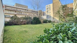 Une cour avec une pelouse verdoyante, quelques arbustes et un bâtiment à étages, doté de balcons.