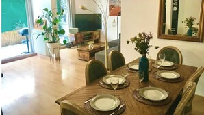 Un coin repas avec une table en bois dressée pour quatre personnes, entourée de chaises. On peut voir un vase rempli de fleurs sur la table, ainsi qu’un grand miroir au mur.